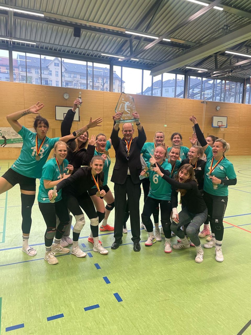 Die 1. Damen jubeln in einer Sporthalle mit Medaillen und dem Meisterpokal der Regionalliga Nordost